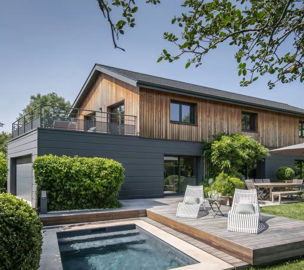 Maison ossature bois Greenkub à étage, bardage bois clair et soubassement anthracite, terrasse en bois côté jardin