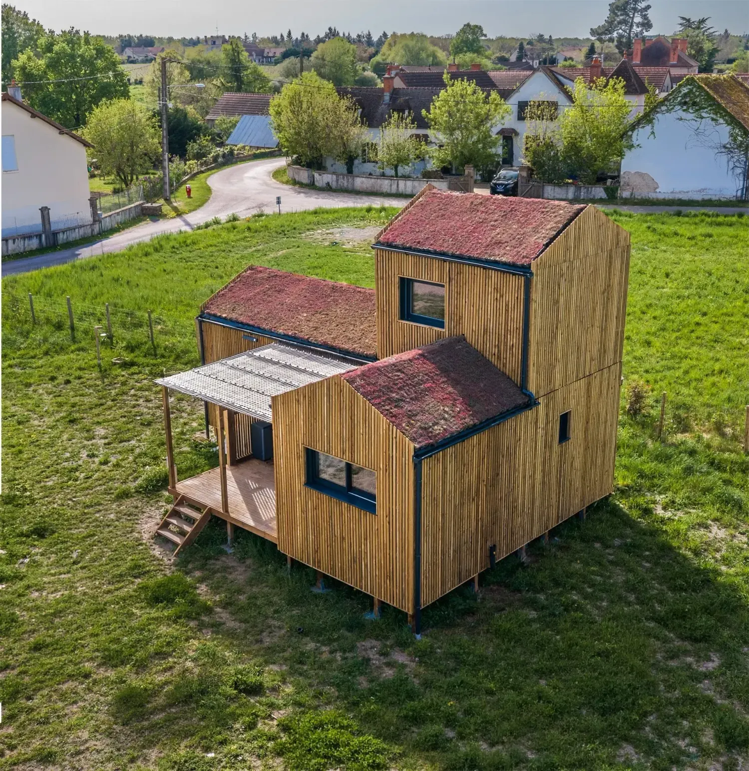 Vue aérienne d’une maison bois Greenkub GK50 en Allier · composition de trois volumes bardage bois vertical avec toitures végétalisées, terrasse centrale couverte, environnement rural