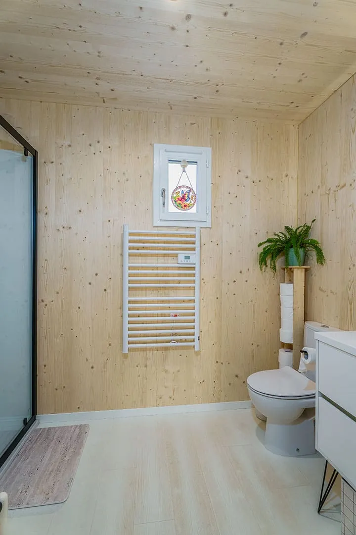 Salle d’eau compacte d’une maison bois Greenkub GK50 · parois en bois massif épicéa naturel, vasque à poser blanche, miroir rétroéclairé, WC suspendu
