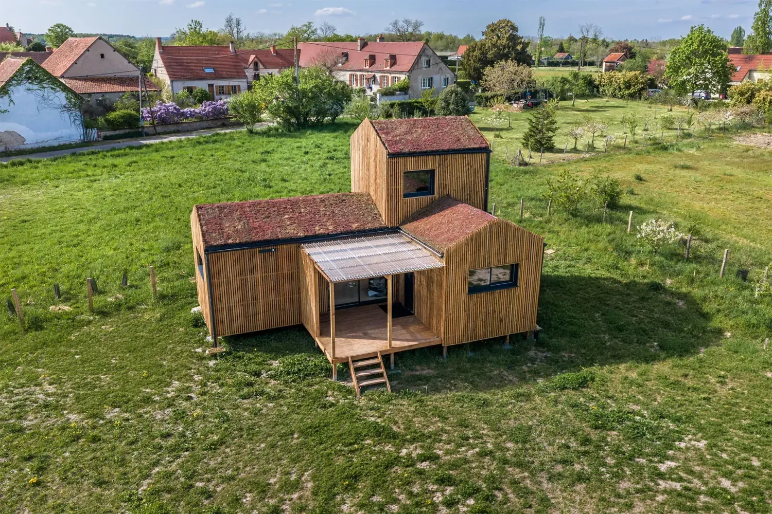 Vue aérienne d’une maison bois Greenkub GK50 en Allier · composition de trois volumes bardage bois vertical avec toitures végétalisées, terrasse centrale couverte, environnement rural