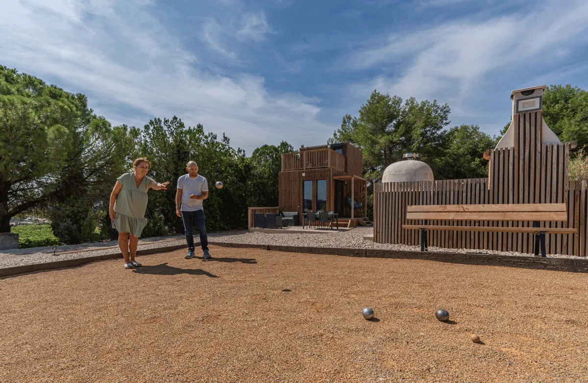 Des personnes jouant à la pétanque devant une maison en bois