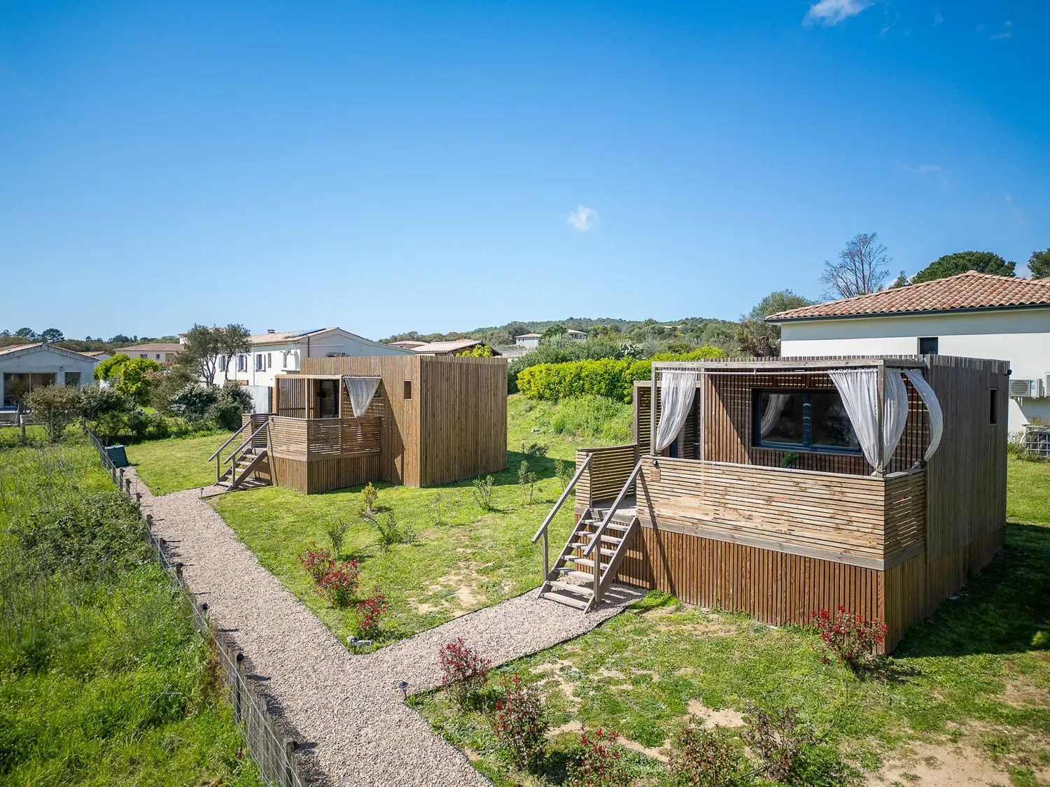 Studio Greenkub GK20 posé sur pilotis bois, terrasse avec rideaux blancs flottants au vent