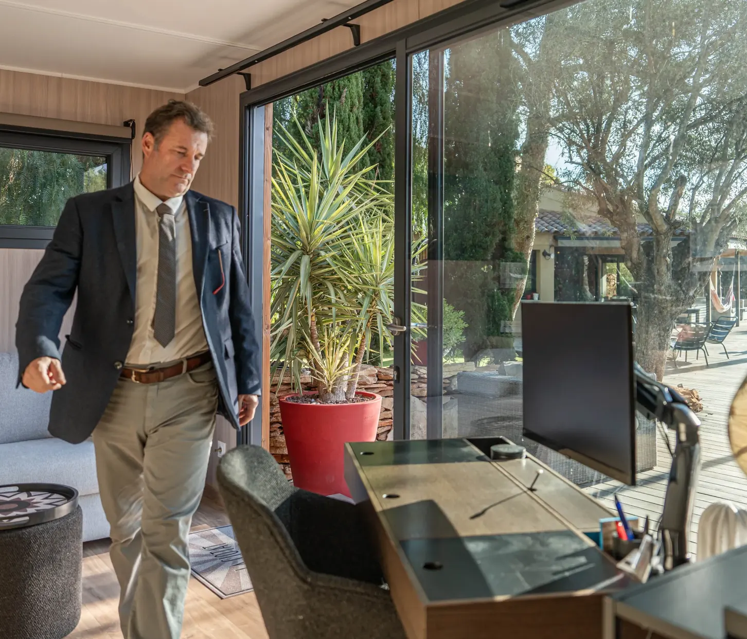 Studio de jardin aménagé en bureau : poste de travail, écran et fauteuil, grande baie vitrée coulissante ouverte sur le jardin